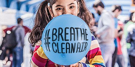 Young girl blows up balloon with wording Breathe Clean Air